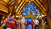 A Cast Member welcomes a female Guest with a flower lei necklace as other Guests stand nearby, smiling
A Cast Member welcomes a female Guest with a flower lei necklace as other Guests stand nearby, smiling