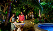 Two women with drinks talk while standing at an outdoor cocktail table near a candlelit stone path
Two women with drinks talk while standing at an outdoor cocktail table near a candlelit stone path