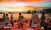 A group of Guests stand on a beach near banquet tables set for an elegant outdoor dinner
A group of Guests stand on a beach near banquet tables set for an elegant outdoor dinner