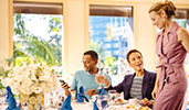 A woman joins a man and a woman at a dining table with a floral centerpiece
A woman joins a man and a woman at a dining table with a floral centerpiece
