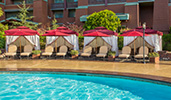Tents and umbrellas provide shade over a row of padded chairs next to a pool
Tents and umbrellas provide shade over a row of padded chairs next to a pool