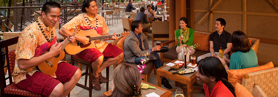 People sit at a restaurant while 2 men play a ukulele and a guitar nearby People sit at a restaurant while 2 men play a ukulele and a guitar nearby