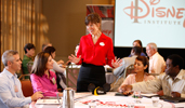 A woman wearing a name tag standing in front of a table of people A woman wearing a name tag standing in front of a table of people