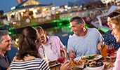 A small group enjoys a family style dinner at an outdoor table overlooking a lake
A small group enjoys a family style dinner at an outdoor table overlooking a lake