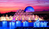 A smiling chef standing behind an illuminated food station at sunset near an active fountain with Spaceship Earth at Epcot in the distance A smiling chef standing behind an illuminated food station at sunset near an active fountain with Spaceship Earth at Epcot in the distance