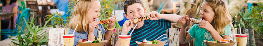 Three kids enjoy kabobs and beverages at an outdoor table Three kids enjoy kabobs and beverages at an outdoor table