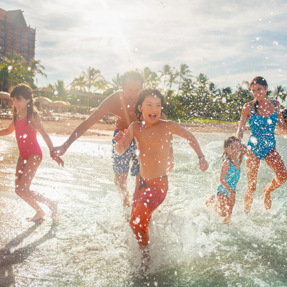 Three kids splashing on the beach with their parents behind them
