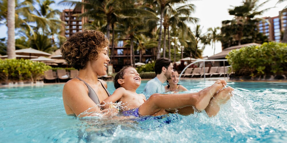 A family of 4 are all smiles while enjoying time in the Waikolohe pool at Aulani Resort