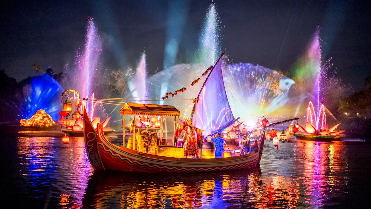 A storyteller dressed in a traditional Asian costume stands on a boat during a light show over a lake