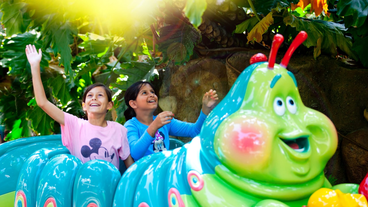Dos niñas sonrientes pasean en la atracción Heimlich's Chew Chew Train en la tierra "a bug's land"