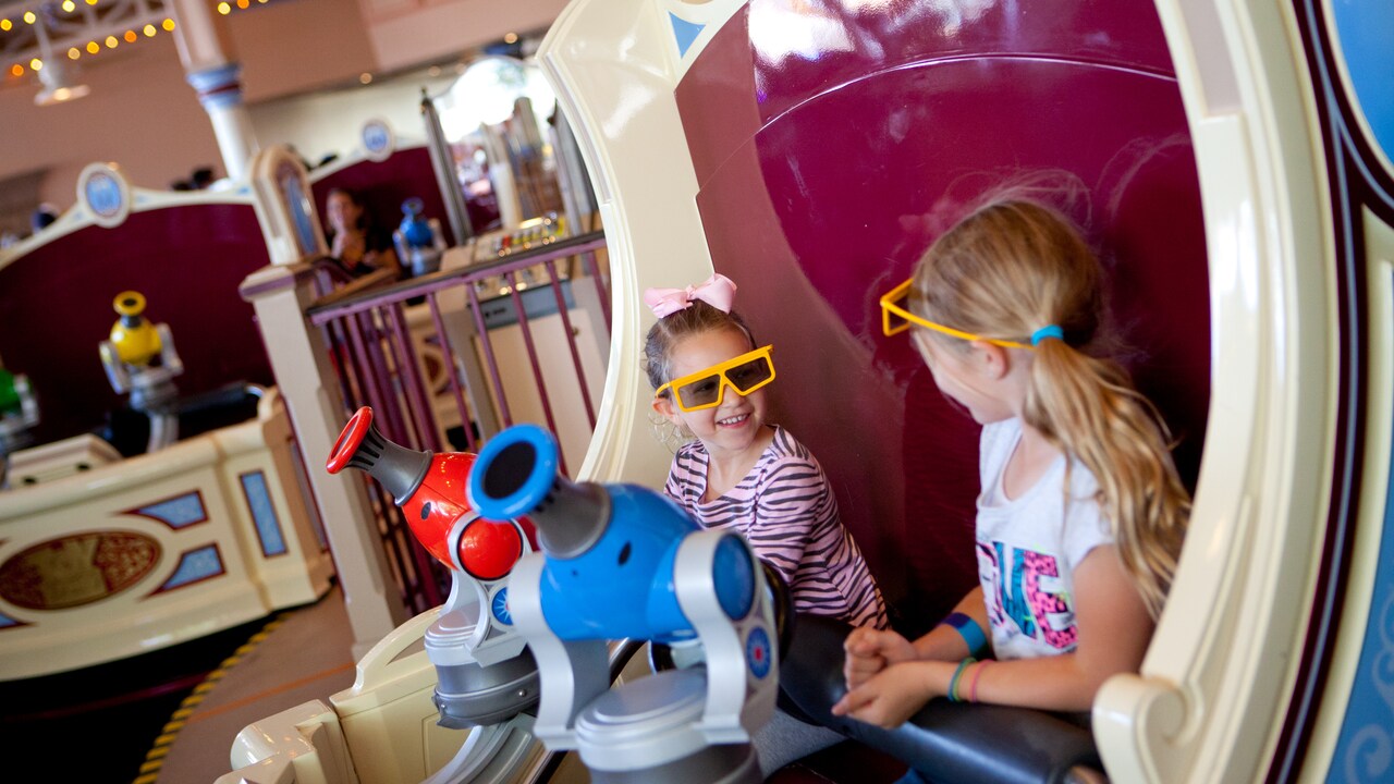 Dos niñas pequeñas van sonrientes en un carro de la atracción Toy Story Midway Mania! con sus lentes de 3D