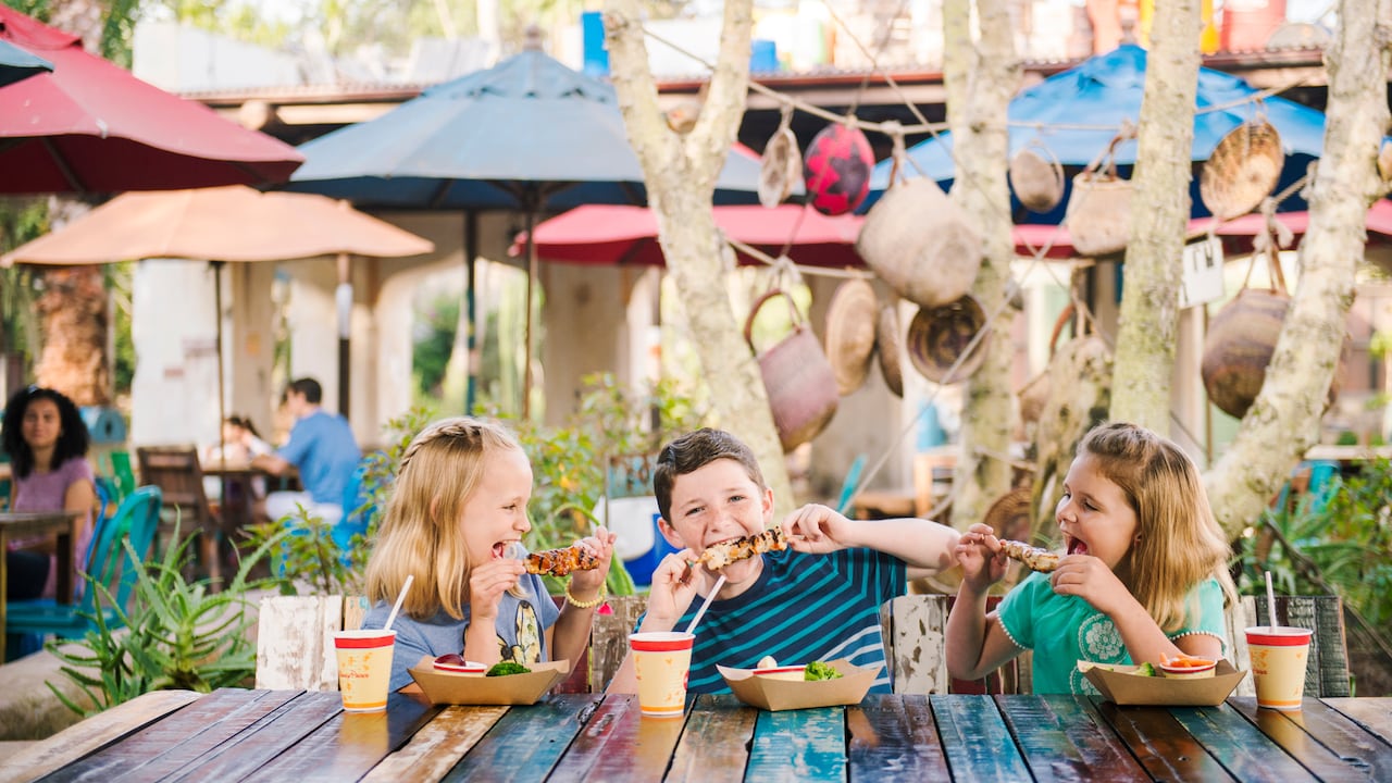 Three kids enjoy kabobs and beverages at an outdoor table