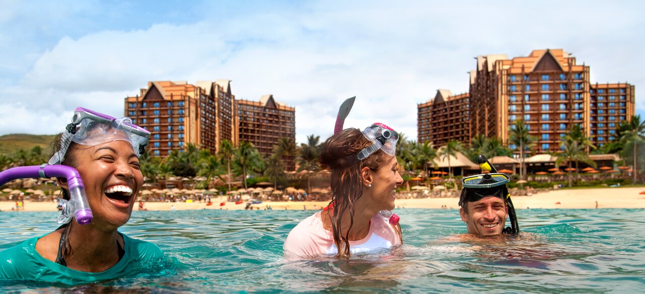 Two young women and a young man with masks and snorkel laugh as they enjoy the ocean at Aulani.