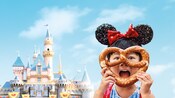 Une fille porte des oreilles de Mickey et tient un bretzel devant le Sleeping Beauty Castle