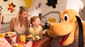 A smiling adult and child enjoying Character Dining with Pluto A smiling adult and child enjoying Character Dining with Pluto
