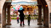 Mickey and boy, both silhouetted, hold hands as they walk through an archway towards Fantasyland