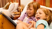 Two young sisters read a book together while relaxing on a bed in their Disney Resort hotel room Two young sisters read a book together while relaxing on a bed in their Disney Resort hotel room