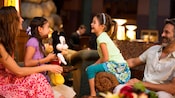 Two little girls sit with their mother and father in the lobby of their hotel and play with a Mickey plush toy Two little girls sit with their mother and father in the lobby of their hotel and play with a Mickey plush toy