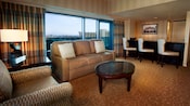 A sitting area with a sofa, easy chair, oval coffee table and, beyond, a bar with 3 stool-chairs