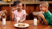 Children sitting at a table enjoy a snack of Mickey cookies and milk