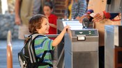 A smiling boy with a backpack at a turnstile entrance to Disney's California Adventure Park