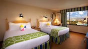 Two queen beds with beach ball pillows, lamps, end table, mounted mirror, desk, chair and window with Disney California Adventure Park view