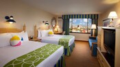 Two queen beds with wooden headboards, a desk, TV-dresser, sofa and, beyond, a window