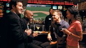 4 young adults enjoy drinks and small bites of food at ESPN Zone while a baseball game plays on a screen behind the bar