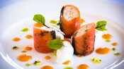 Smoked salmon strips wrapped around a creamy salmon mousse on a plate adorned with 3 kinds of sauce