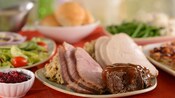 Portions of beef, sliced ham and turkey fill a platter surrounded by plates with various side dishes