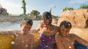 2 boys smile and a woman shouts in excitement as water splashes them