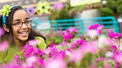 A smiling girl wearing glasses and a floral headband sits within a garden exhibit