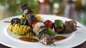 2 grilled beef shish kabobs served on a plate with seasoned rice