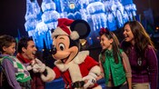 Papai Noel Mickey de mãos dadas com uma família vestida para a estação com luzes brilhando no Castelo da Cinderela
