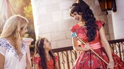 Princess Elena of Avalor shows her jeweled scepter to a smiling little girl wearing an Elena costume