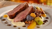 A plate containing slices of roast duck leg atop a bed of puree beside florets of cauliflower and a wedge of cooked peach