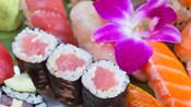 Three pieces of sushi presented beside sashimi and a flower garnish