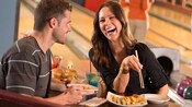A man and a woman enjoy drinks, sushi and hamburger sliders at a bowling alley
