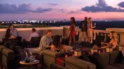 Several people socializing and drinking wine on a rooftop patio at dusk