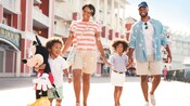 A family of 4 holds hands while happily strolling along Disney’s BoardWalk at Walt Disney World Resort