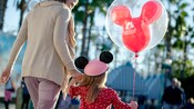 A mother holds hands with her daughter who wears a Minnie Hat and has a Mickey balloon A mother holds hands with her daughter who wears a Minnie Hat and has a Mickey balloon