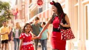 Mother and daughter holding hands and walking together while dressed in Minnie Mouse-themed apparel