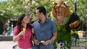 A couple smiles at each other near a topiary display inspired by Disney’s Beauty and the Beast