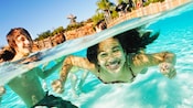 A boy in a pool looks on as a girl swims underwater at Typhoon Lagoon Water Park