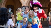 A Disney PhotoPass photographer snaps a picture of a family of six posing with Captain Hook