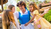 Belle in her blue dress greets 3 young girls, one who’s wearing Belle’s golden ball-gown