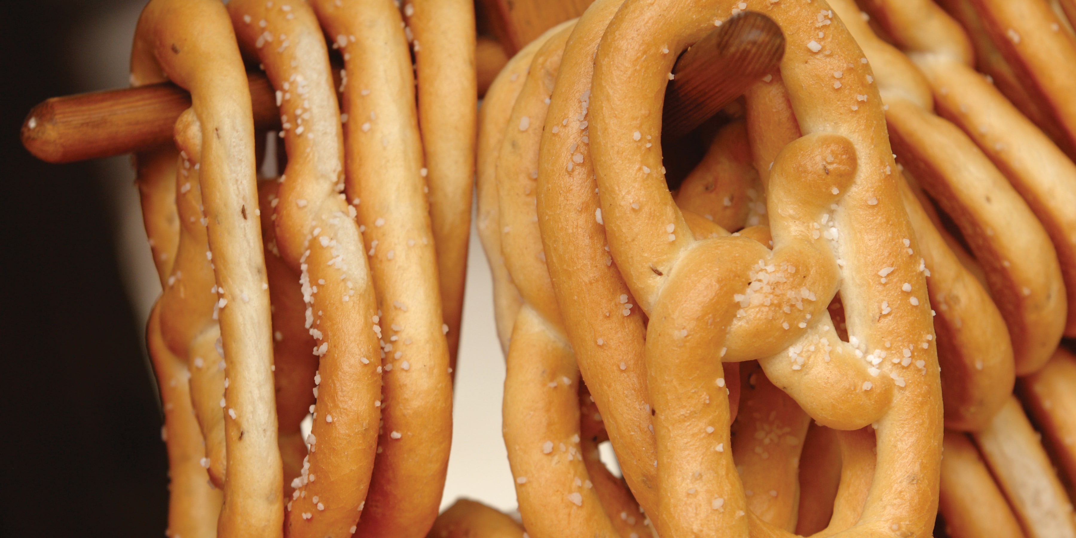 A batch of fresh baked prazels lightly salted hang on a wooden rack