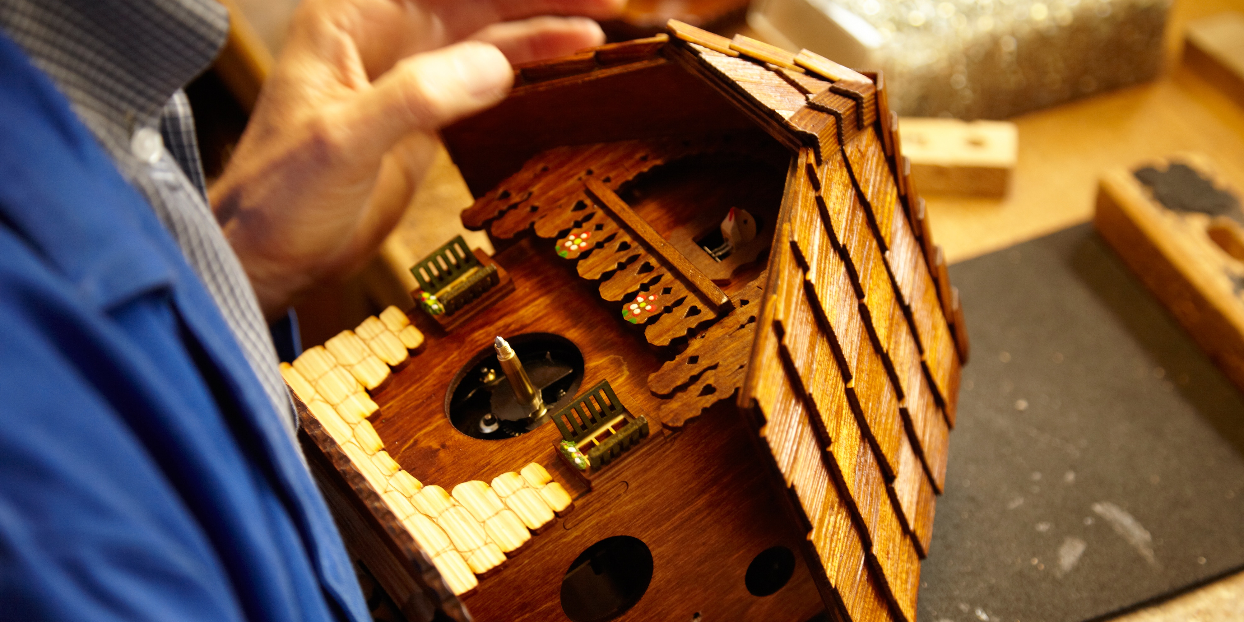 A man holds a carved wooden cuckoo clock, shaped like a house