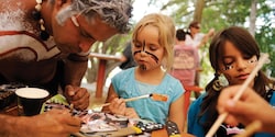 2 girls paint boomerangs with an Aboriginal artist
