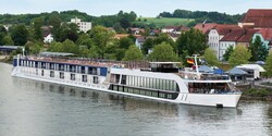 A modern ferry flying the German flag stops at a port in front of green, rolling hills